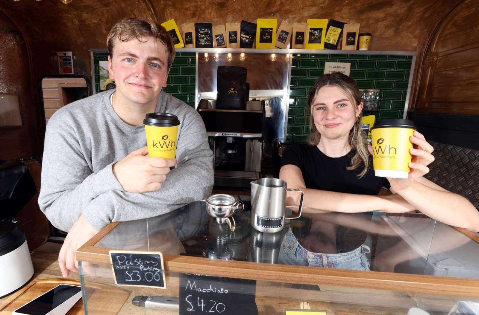 Caitlin and Shaun behind the bar of the kWh horsebox holding kWh coffee cups