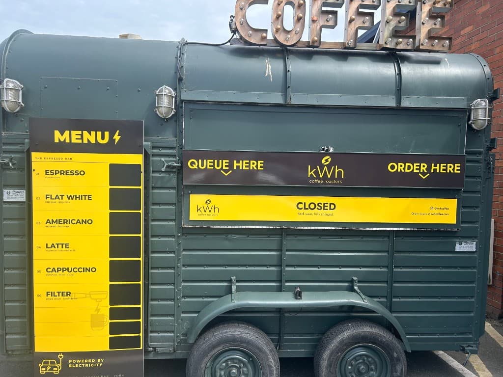 The same horsebox rebranded in kWh charcoal and electric yellow, with the bold 'POWERED BY ELECTRICITY' menu