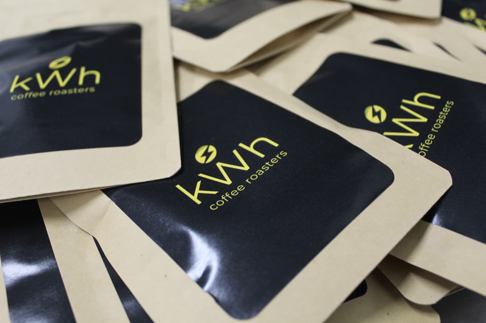 A pile of kWh Coffee Roasters sample bags in kraft and black