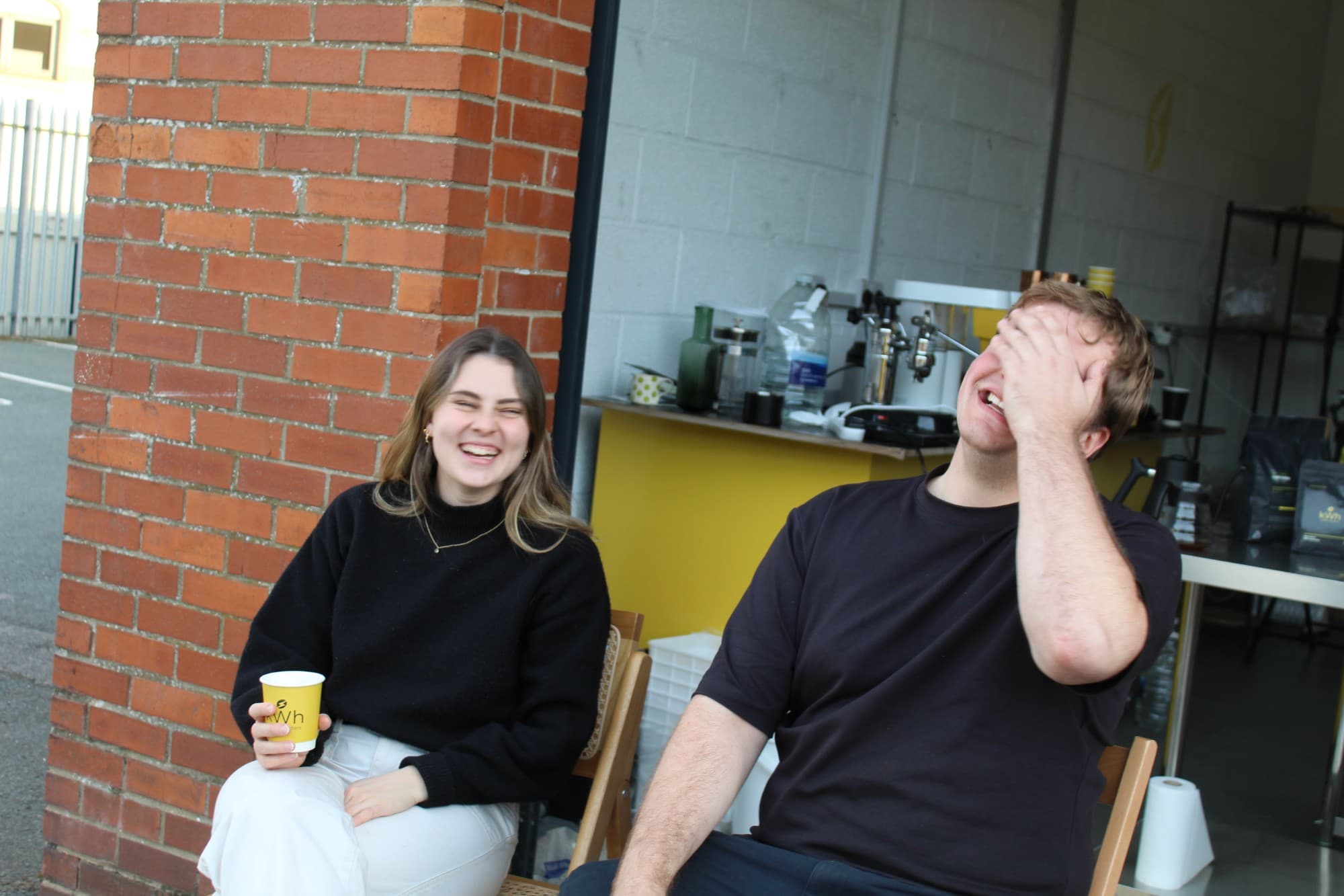 Caitlin and Shaun laughing outside the roastery in York, Caitlin holding a kWh cup